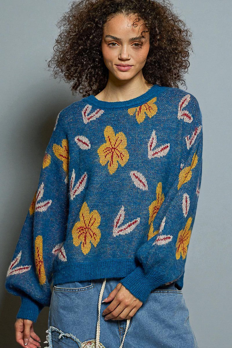 Woman wearing a blue sweater with floral patterns against a gray background