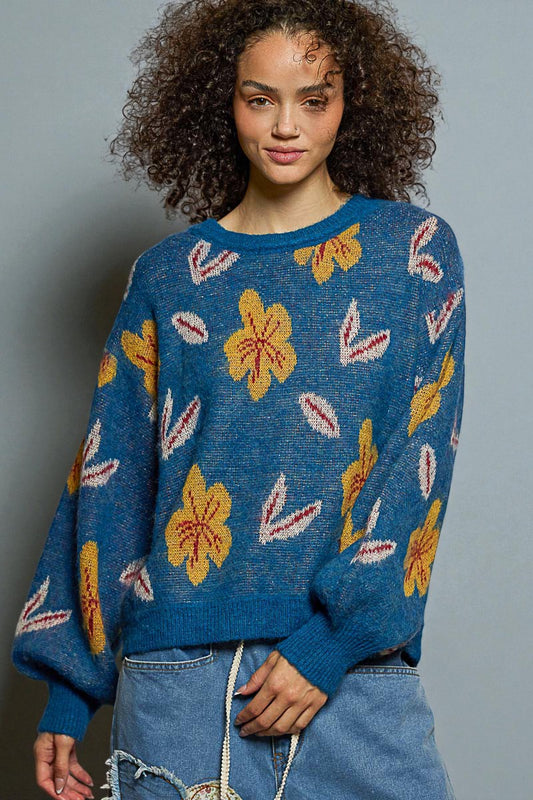 Woman wearing a blue sweater with floral patterns against a gray background