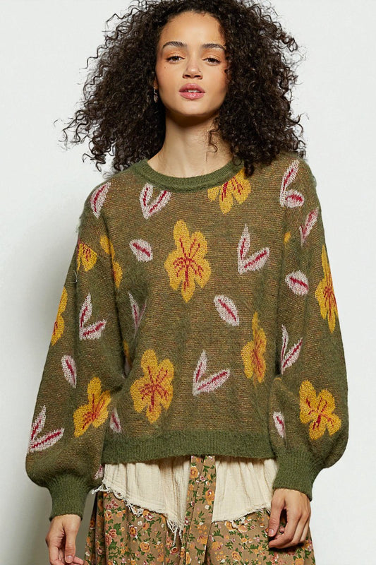 Woman wearing a green sweater with floral patterns on a plain background