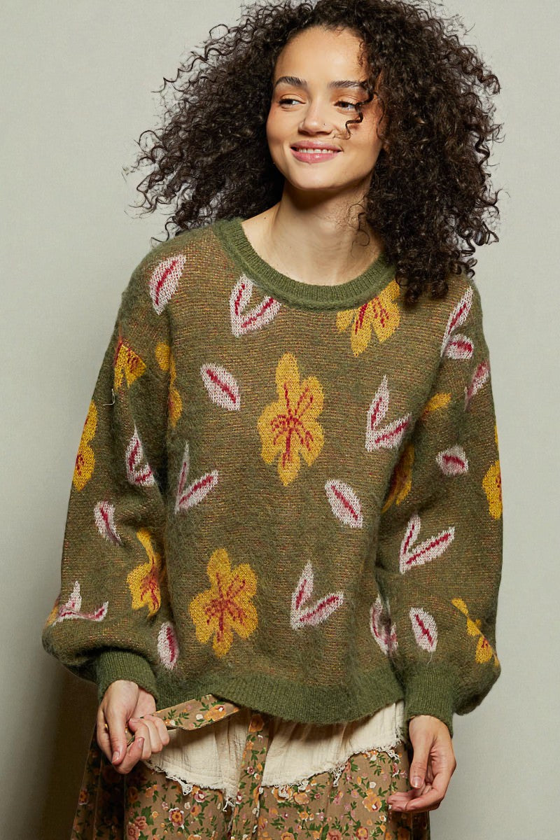 Woman wearing a green sweater with floral patterns against a plain background