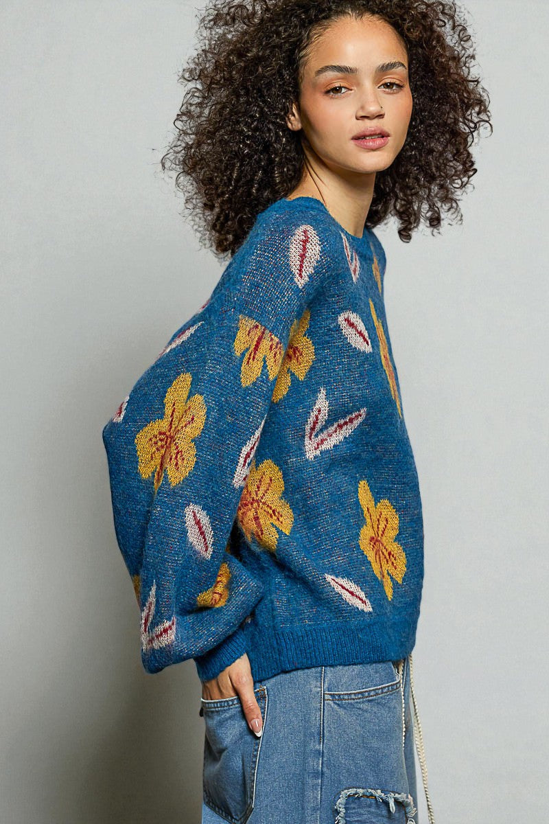Woman wearing a blue sweater with floral patterns against a plain background
