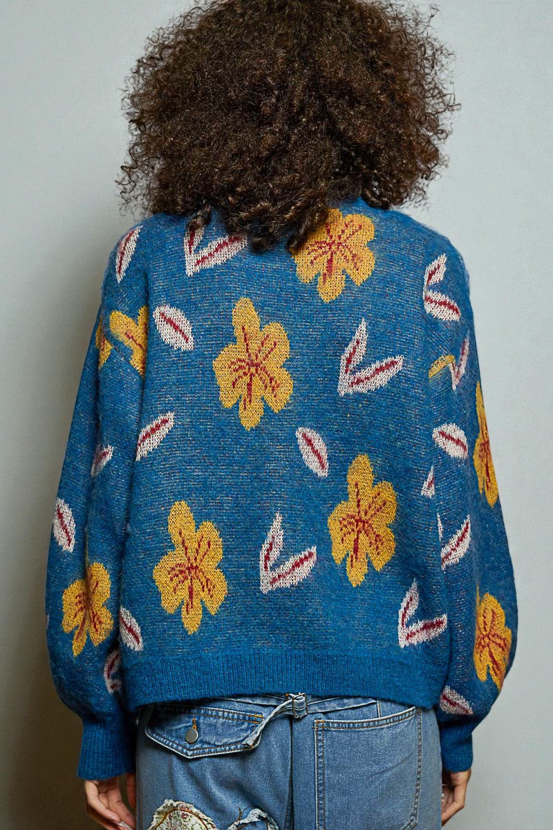 Person wearing a blue sweater with yellow floral patterns against a plain background