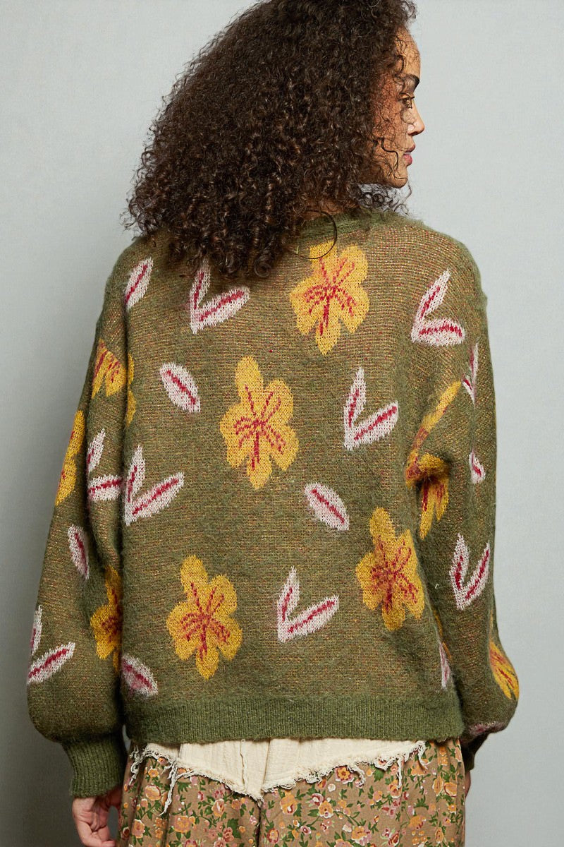 Person wearing a green sweater with floral patterns on a plain background