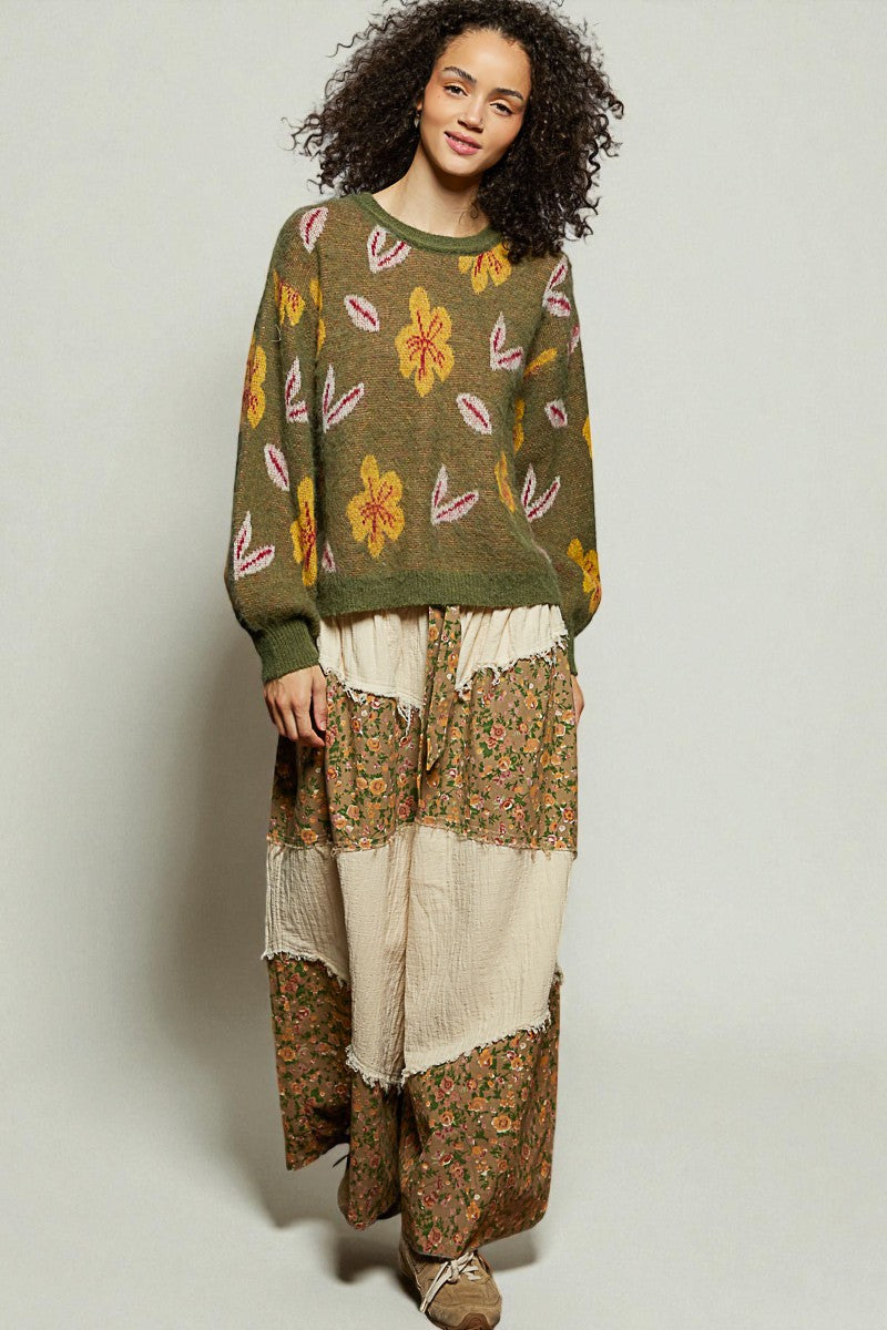 Woman wearing a floral sweater and patchwork pants on a plain background