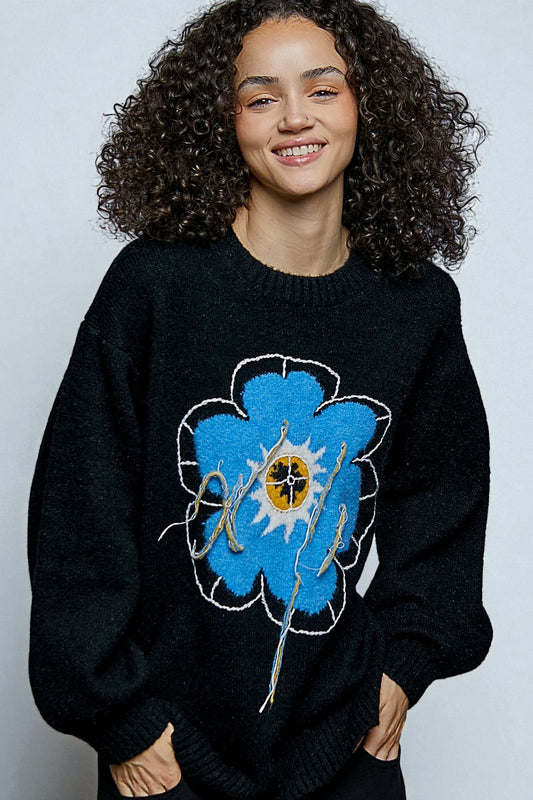 Person wearing a black sweater with a blue flower design on a plain background
