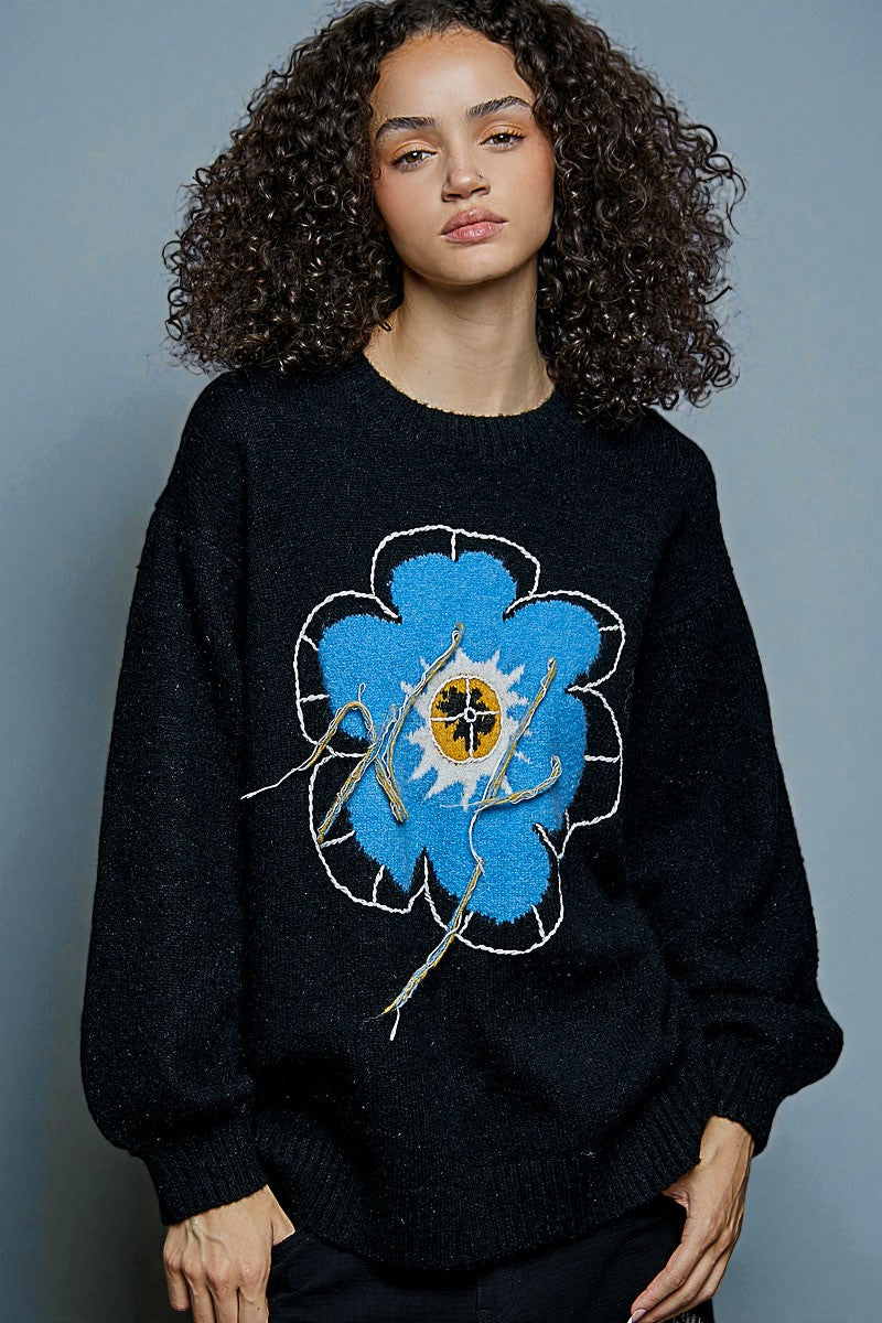 Person wearing a black sweater with a blue floral design on a gray background