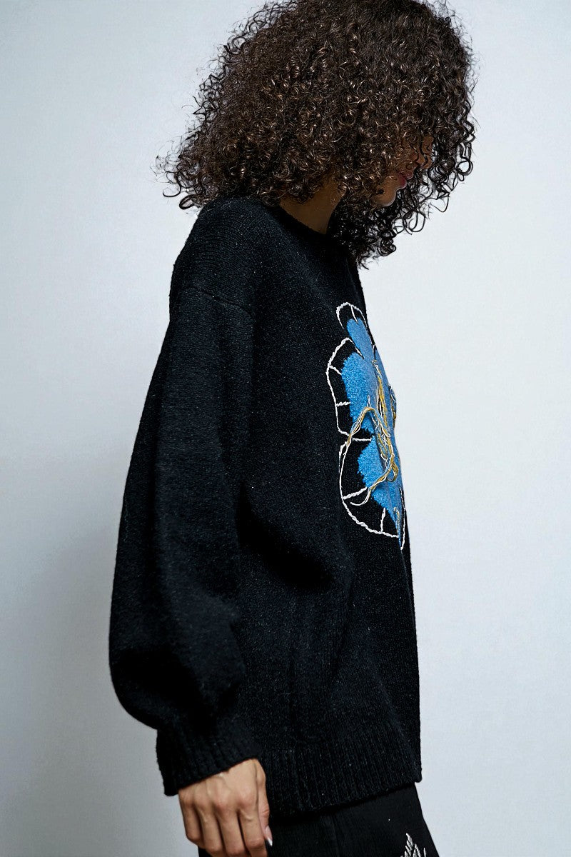 Person wearing a black sweater with a blue graphic design on a plain background