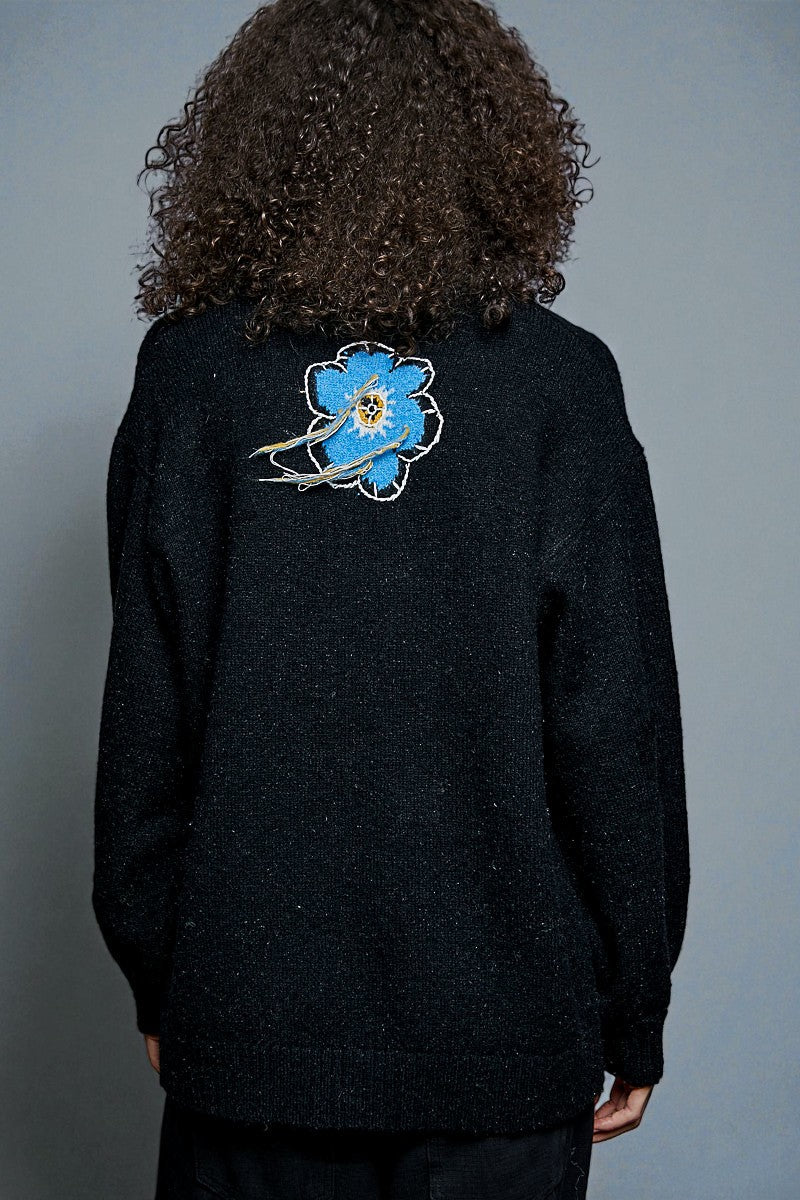 Person wearing a black sweater with a blue floral design on the back against a gray background