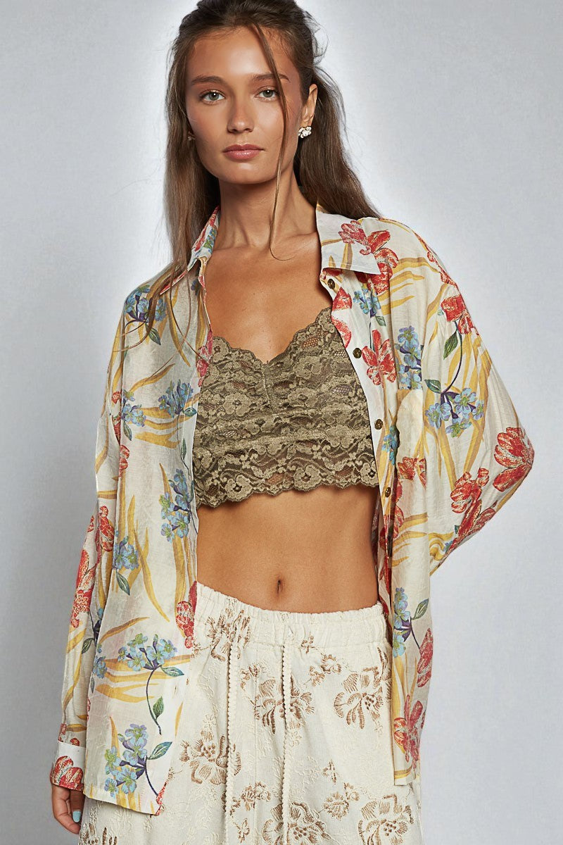 Woman wearing a floral kimono over a lace top and white pants on a gray background