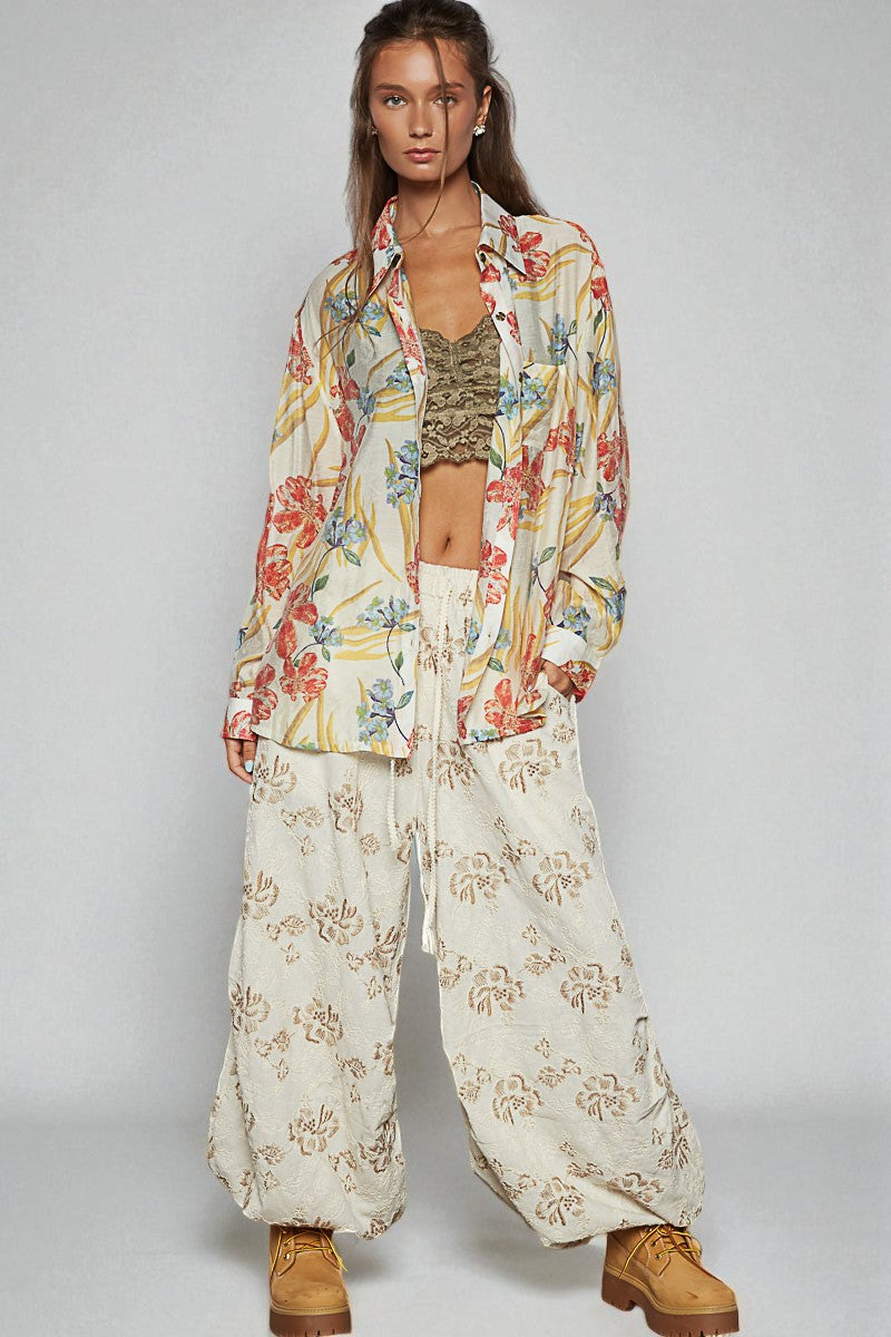 Woman wearing a floral outfit with wide-leg pants and a jacket on a plain background