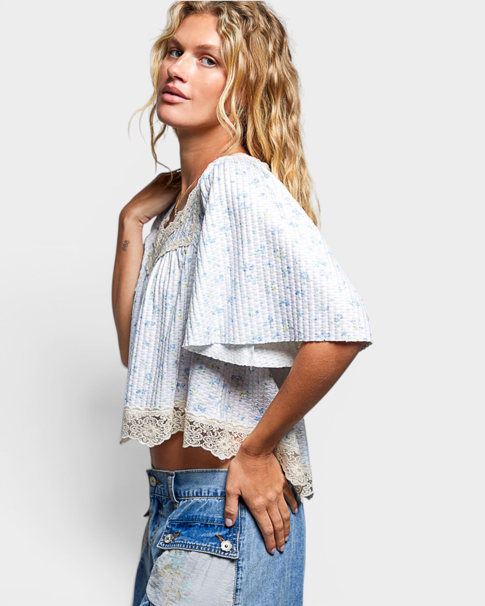 Woman wearing a light blue patterned top and denim shorts on a plain background