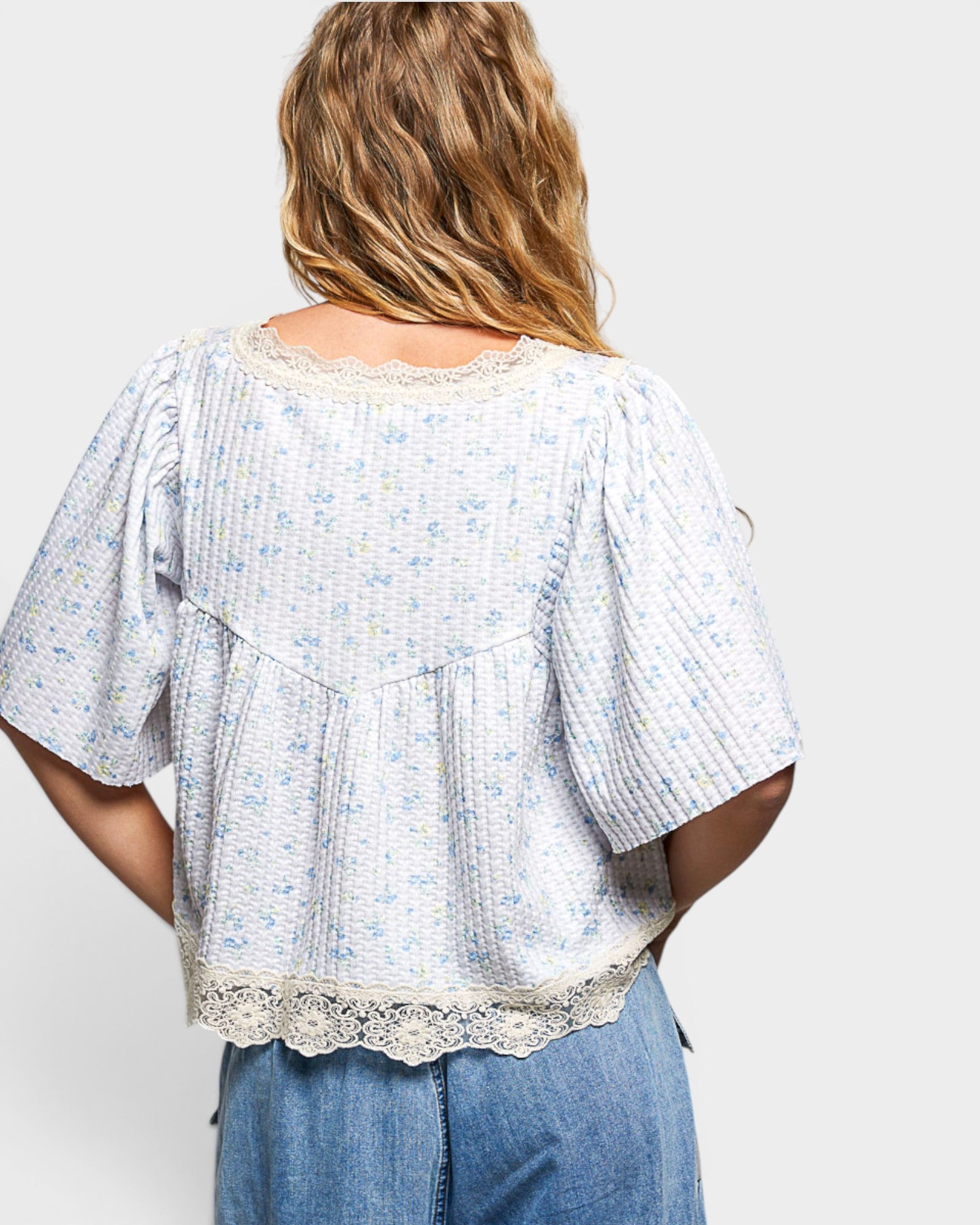 Person wearing a light blue floral blouse with lace trim on a white background