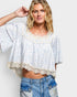 Woman wearing a light blue floral blouse with lace details and denim shorts on a white background