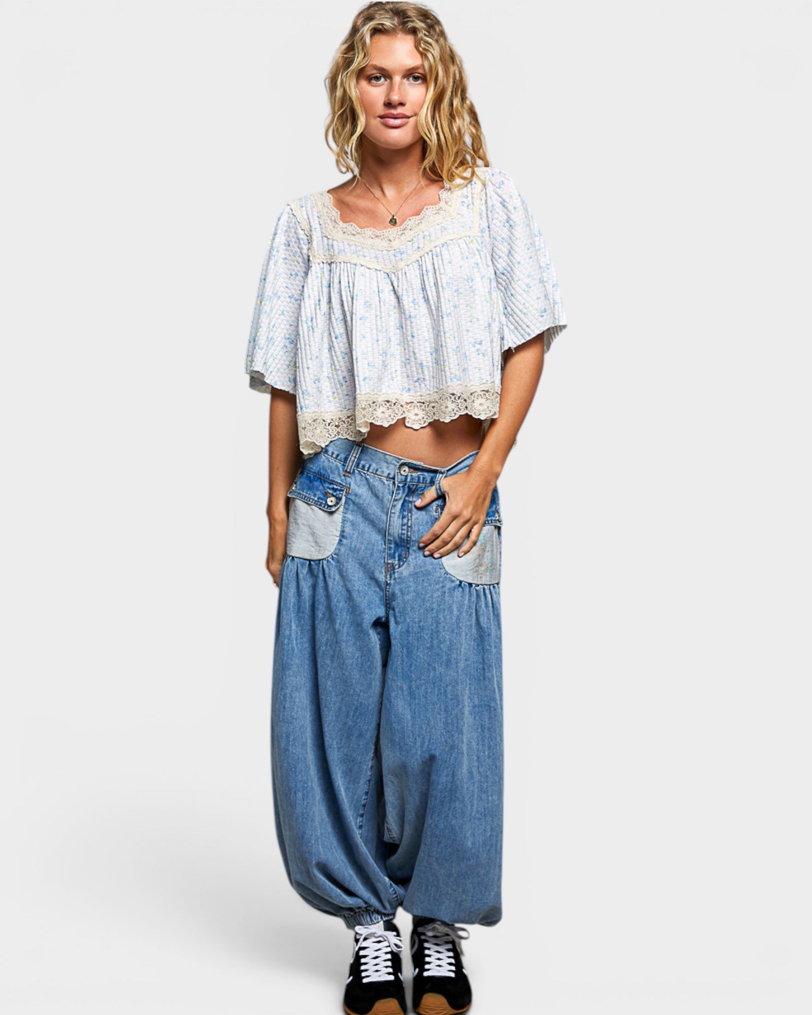 Woman wearing a light blue patterned top and denim baggy pants on a white background
