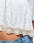Close-up of a floral blouse with lace trim and denim jeans.