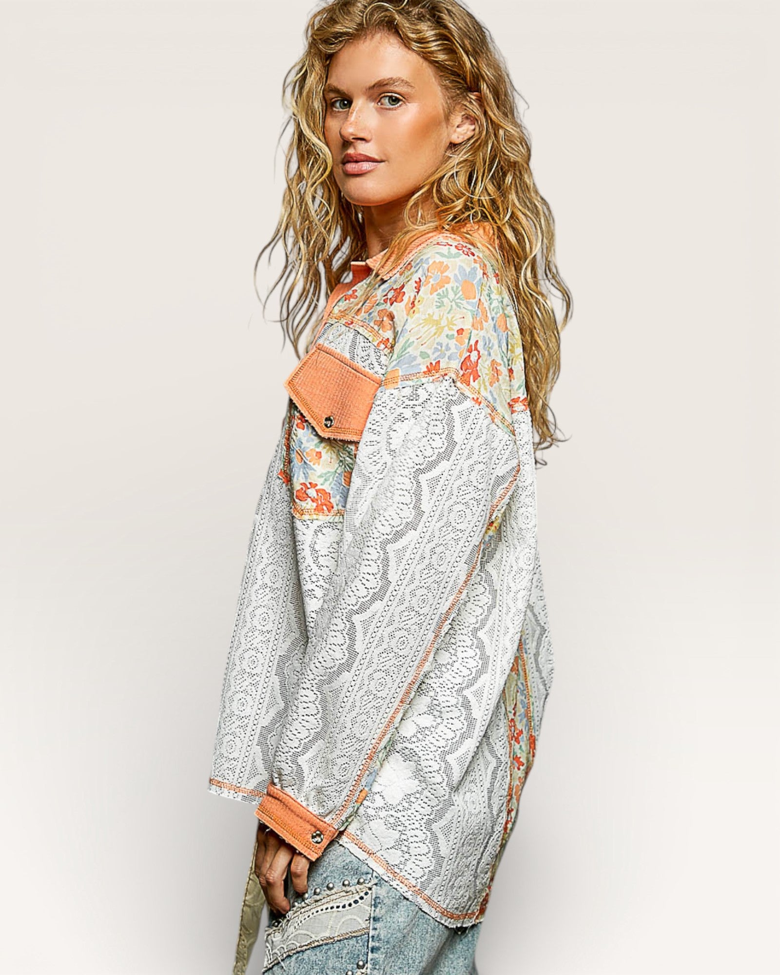 Woman wearing a floral blouse with a lace overlay and denim jacket on a plain background