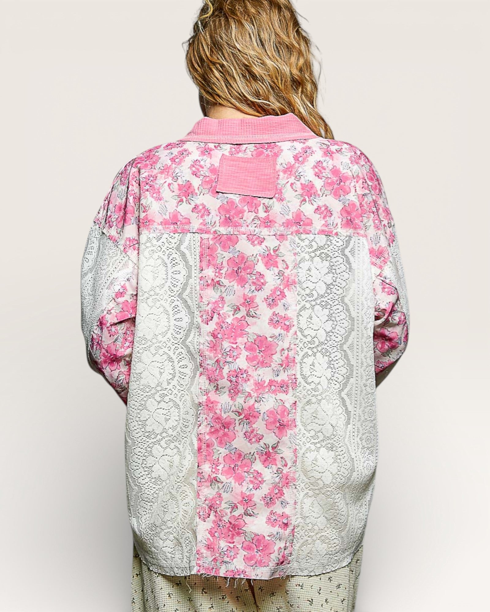 Person wearing a pink floral kimono-style garment with lace details on a plain background