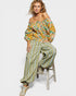 Woman sitting on a stool wearing a floral off-shoulder top and wide-leg pants with a white background