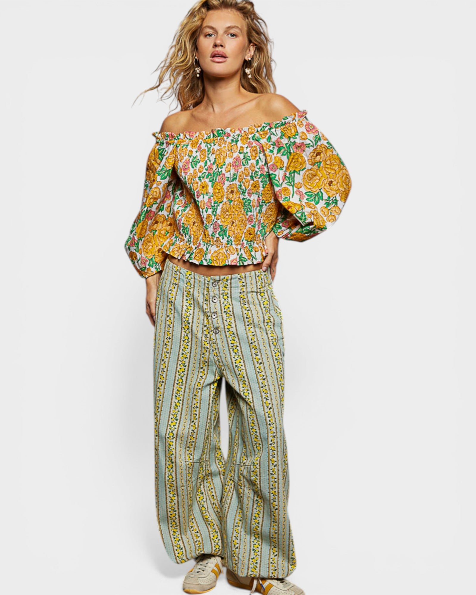 Woman wearing a floral off-shoulder top and wide-leg pants on a white background