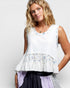 Woman wearing a white sleeveless top with floral details on a plain background