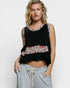 Woman wearing a black sleeveless top with floral patterns and light gray pants on a white background