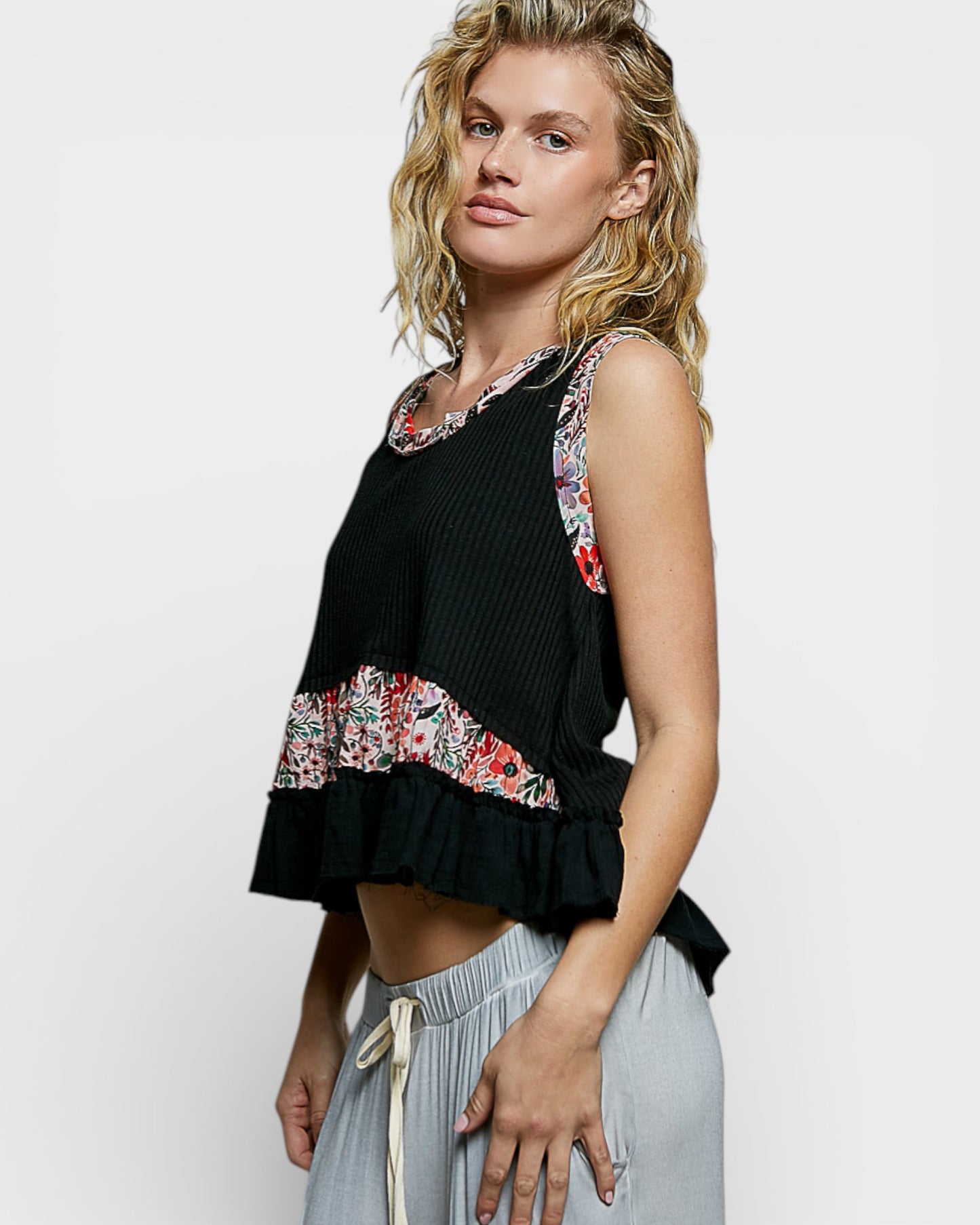 Woman wearing a black sleeveless top with floral patterns and light gray pants on a white background