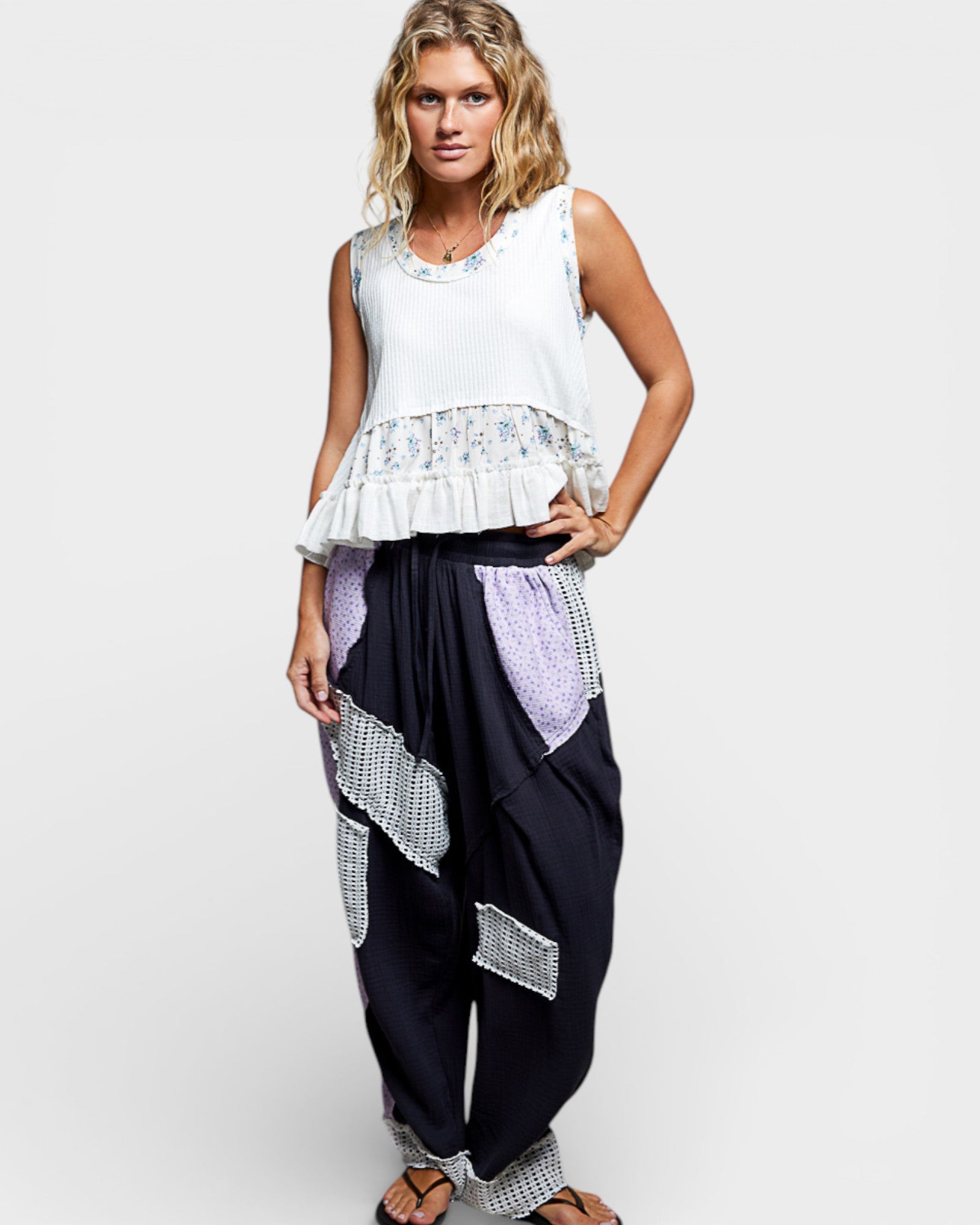 Woman wearing a white top with ruffled details and black pants with geometric patterns on a white background