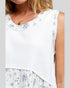 White sleeveless top with floral details worn by a person on a light gray background