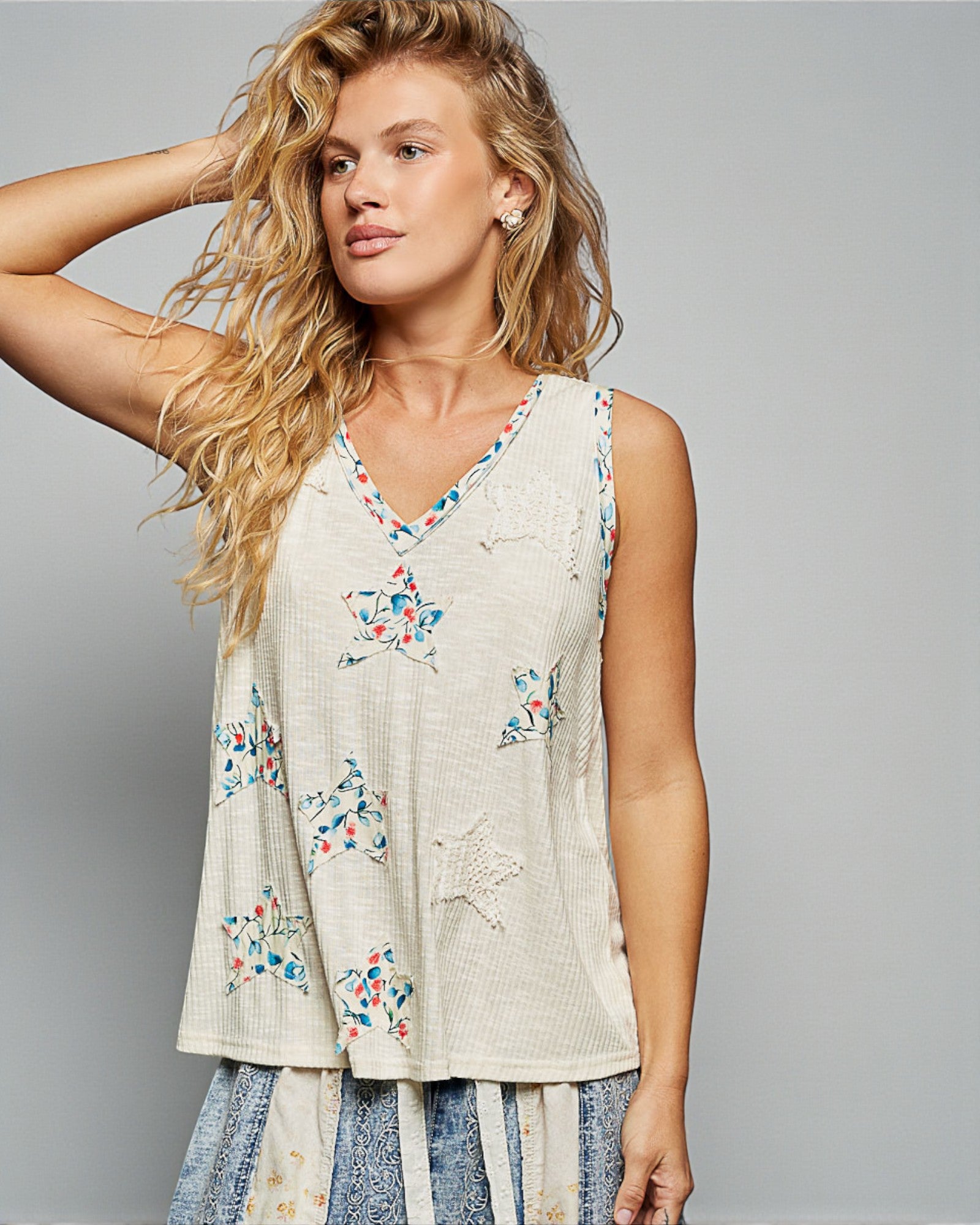 Woman wearing a sleeveless top with floral embroidery against a gray background