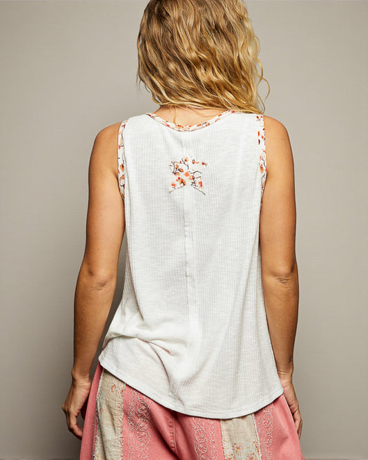 Woman wearing a white sleeveless top with floral embroidery on a beige background