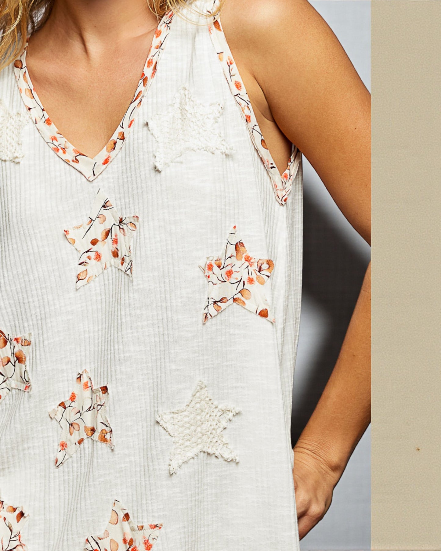 White sleeveless top with floral embroidery on a neutral background