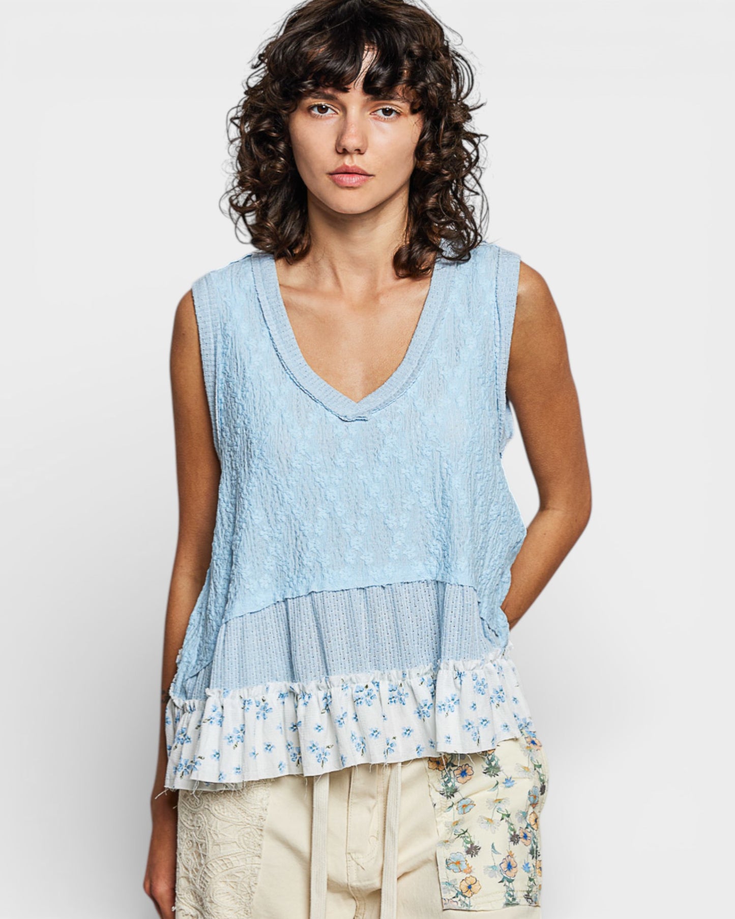 Woman wearing a light blue sleeveless top with floral details on a white background