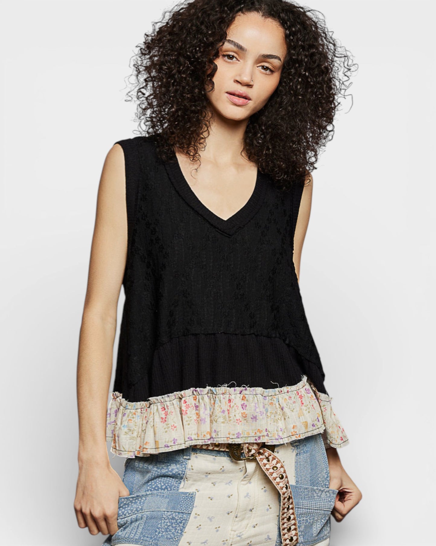 Woman wearing a black sleeveless top with a ruffled bottom on a white background