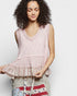Woman wearing a pink sleeveless top with ruffled details on a plain background