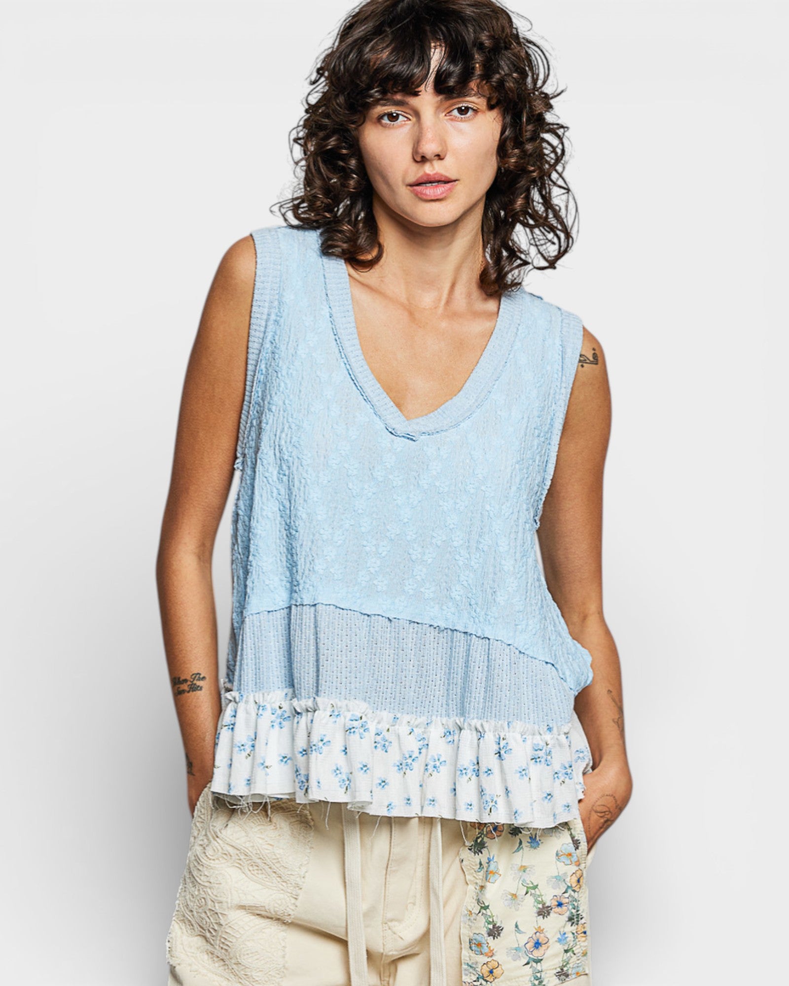 Woman wearing a light blue sleeveless top with floral hem on a white background