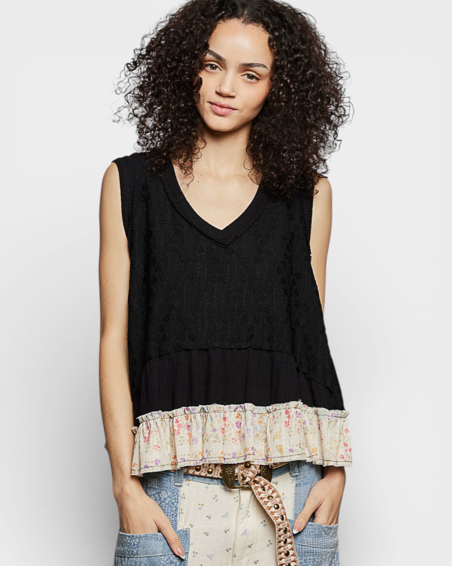 Woman wearing a black sleeveless top with a floral hem against a white background