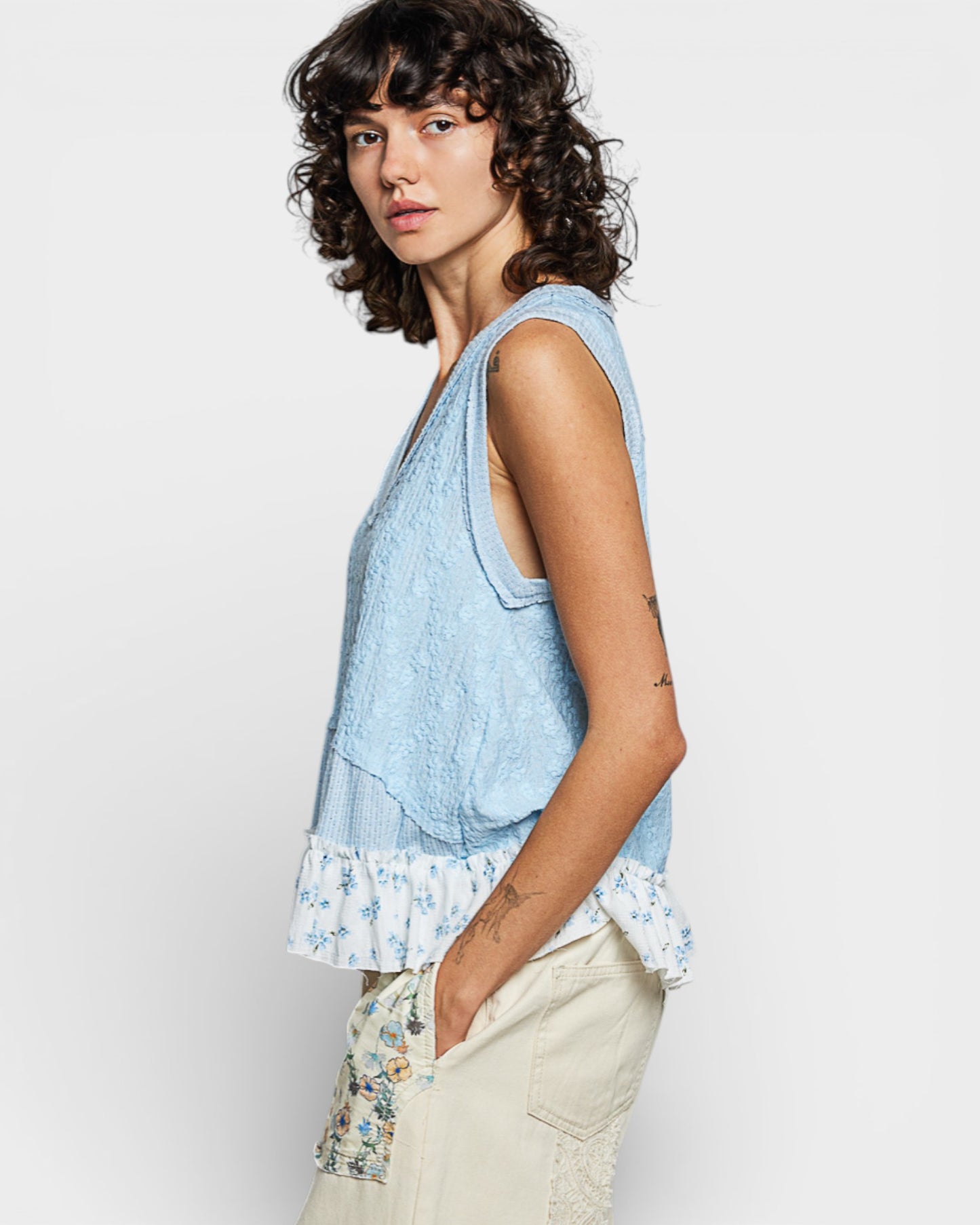 Woman wearing a light blue sleeveless top with floral pants on a white background