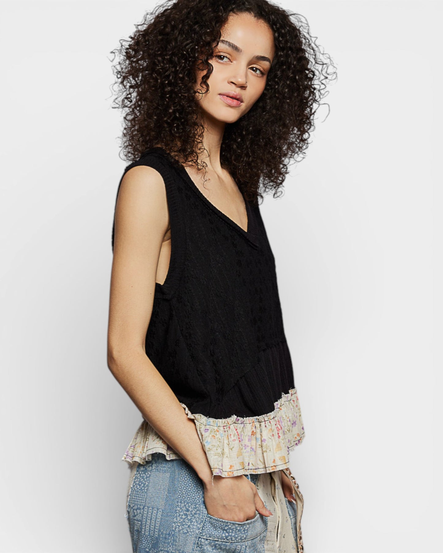 Woman wearing a black sleeveless top with ruffled trim against a white background