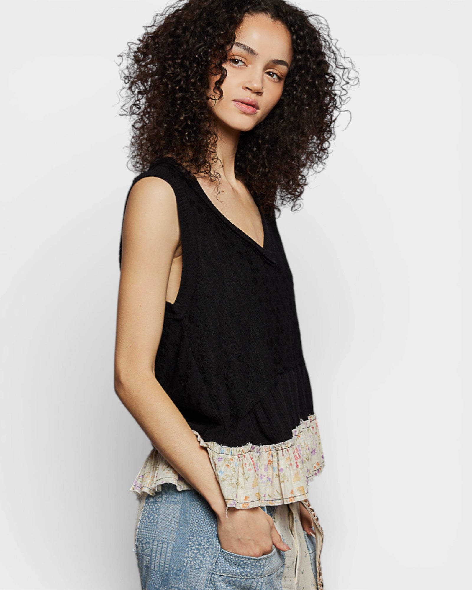 Woman wearing a black sleeveless top with ruffled trim against a white background