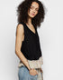 Woman wearing a black sleeveless top with ruffled trim against a white background
