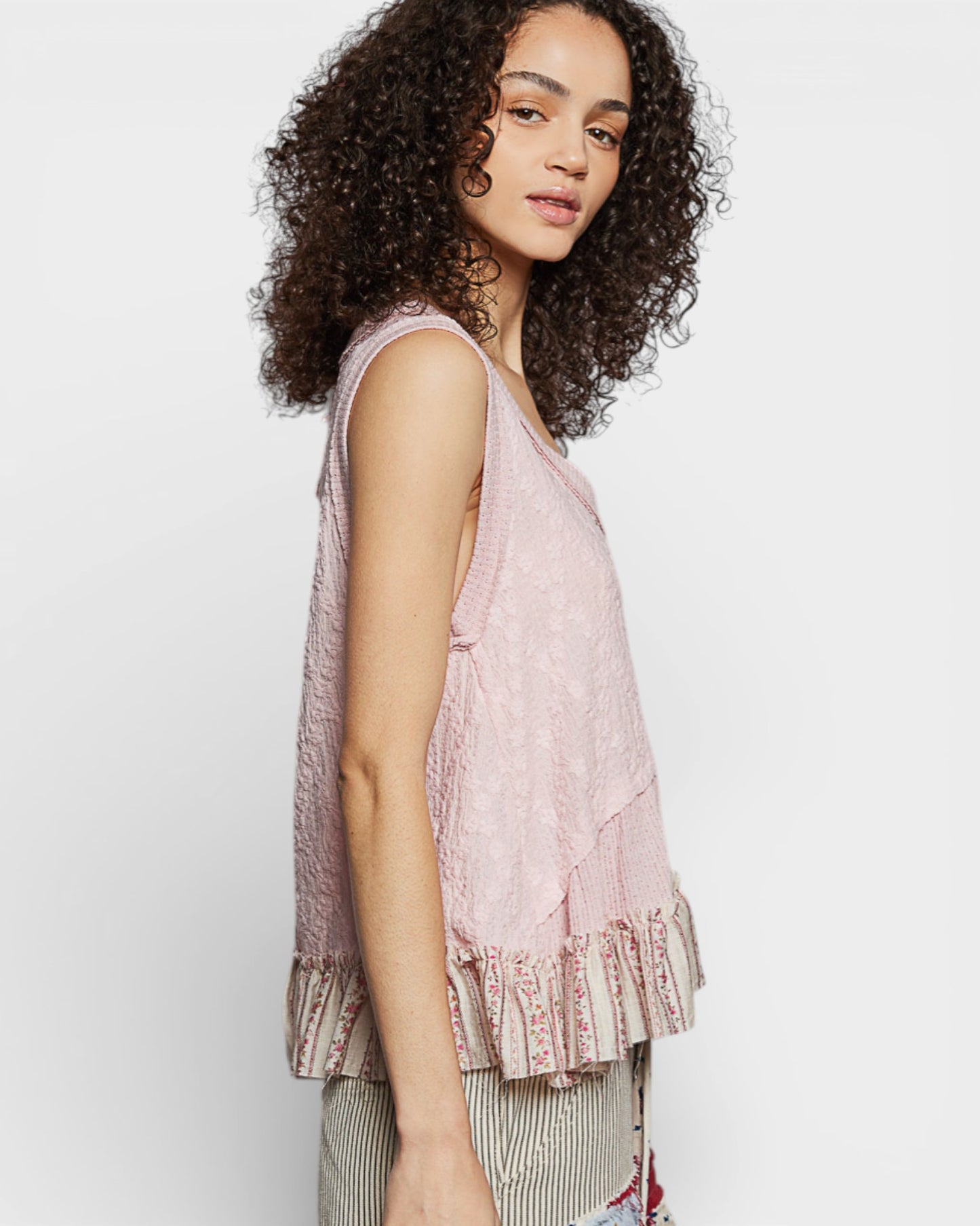 Woman wearing a light pink sleeveless top with ruffled details on a white background