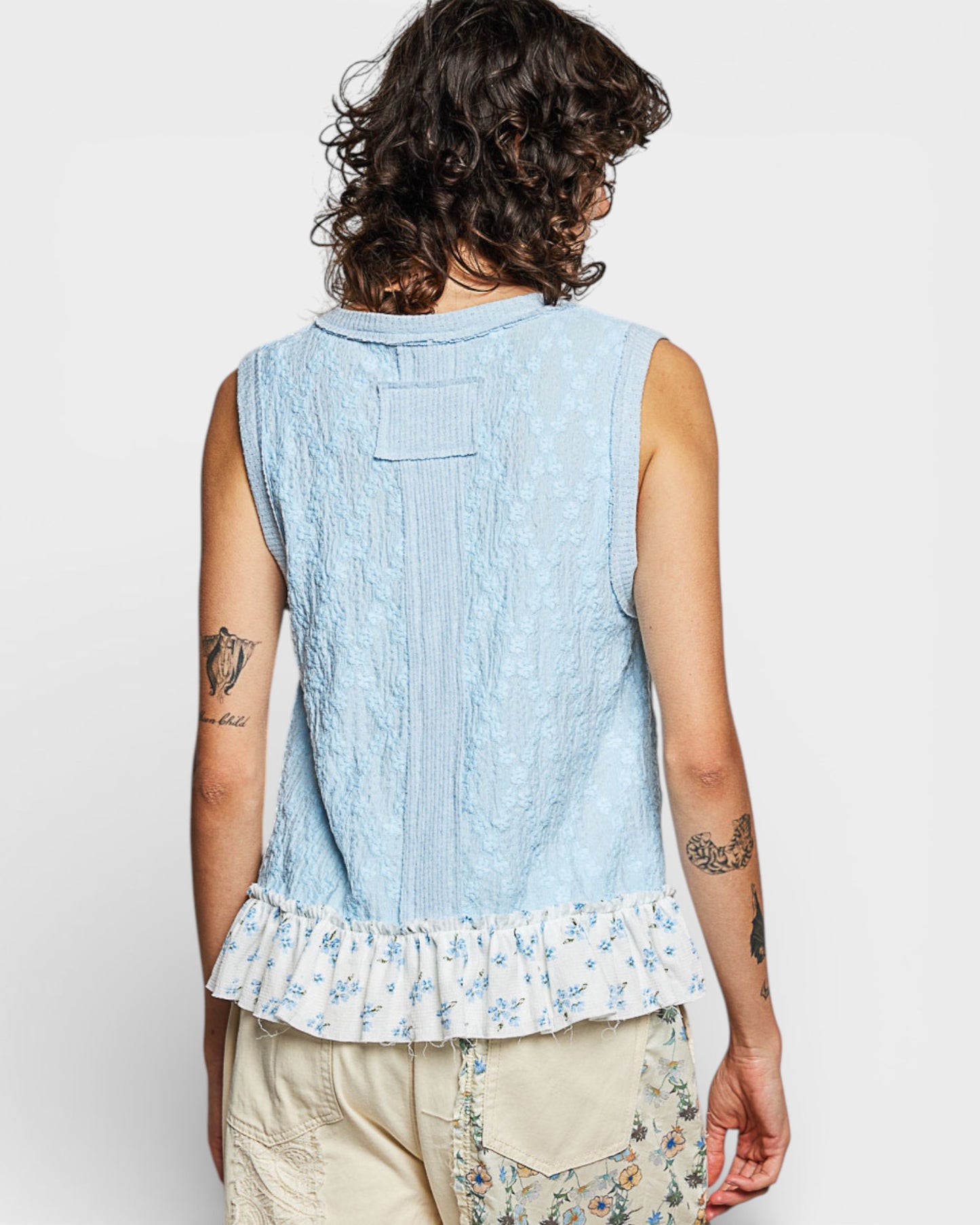 Person wearing a light blue sleeveless top with floral hem on a white background