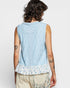 Person wearing a light blue sleeveless top with floral hem on a white background