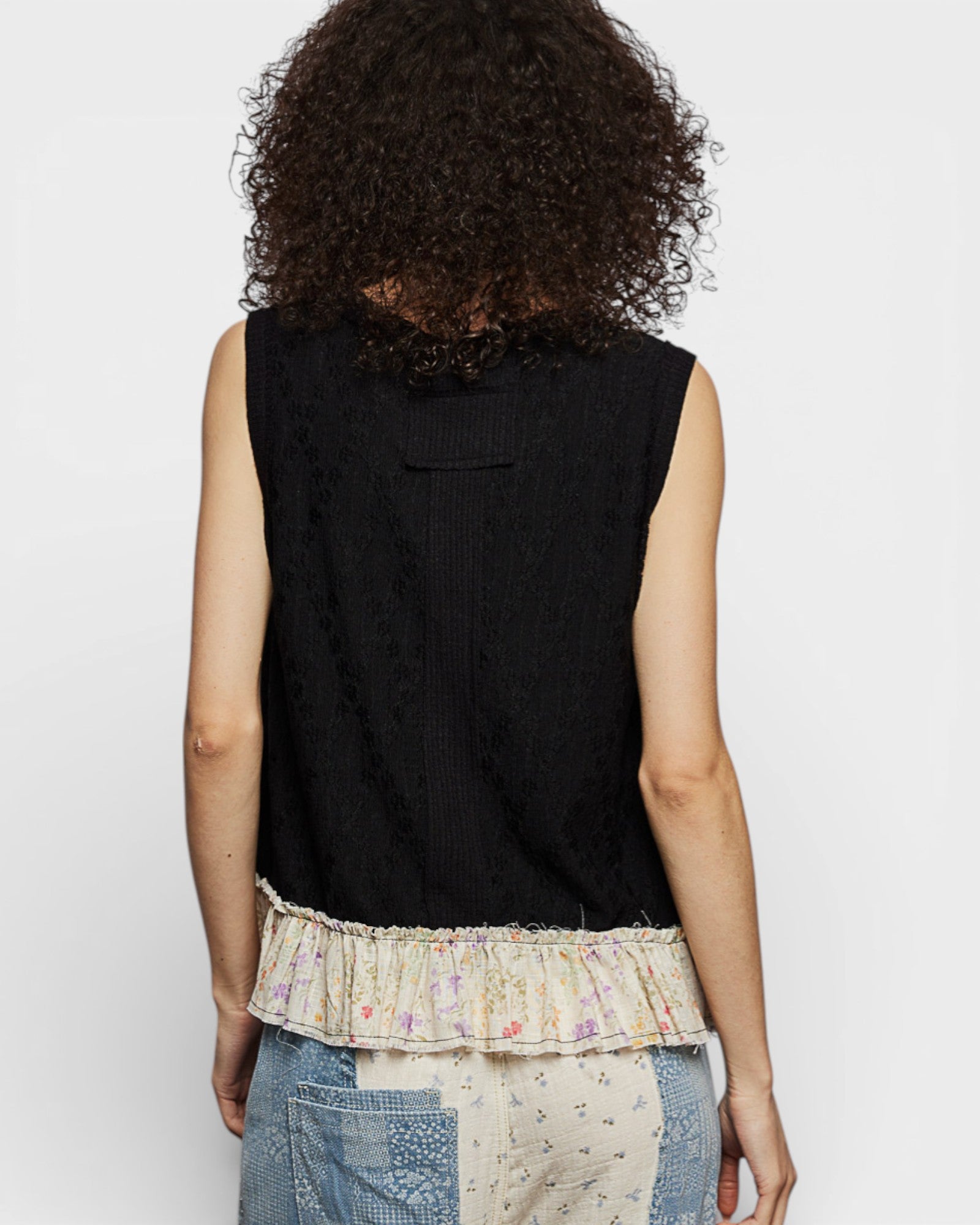 Person wearing a black sleeveless top with a decorative hem on a plain background