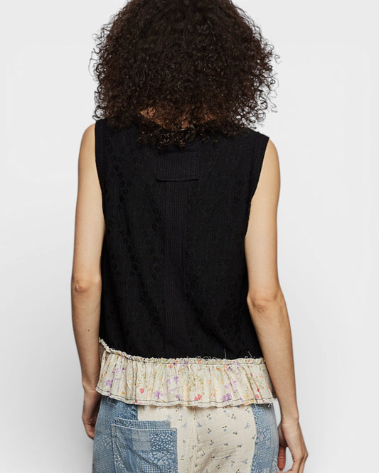 Person wearing a black sleeveless top with a decorative hem on a plain background