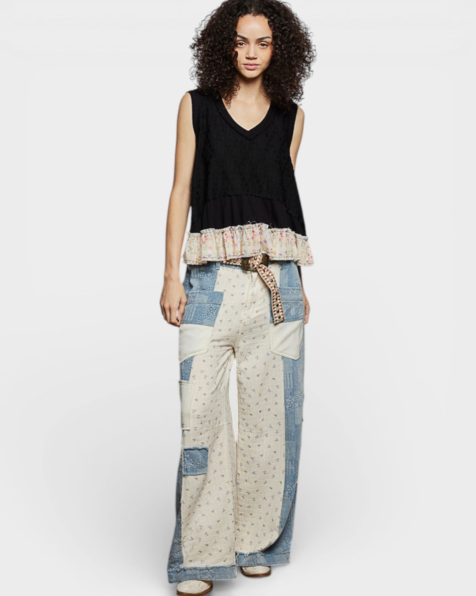 Woman wearing a black sleeveless top and patterned pants on a white background