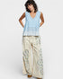 Woman wearing a light blue sleeveless top and beige pants with floral patterns on a white background