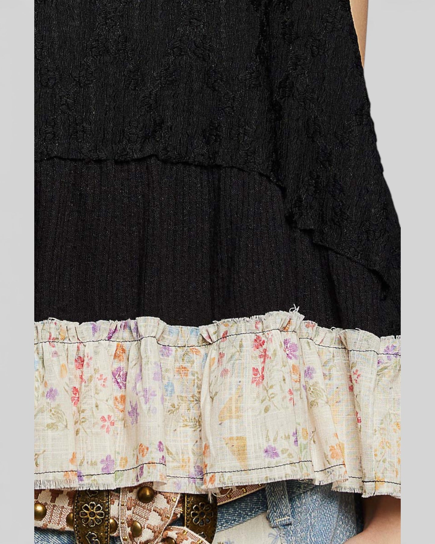 Black top with floral ruffled hem and denim jeans on a neutral background