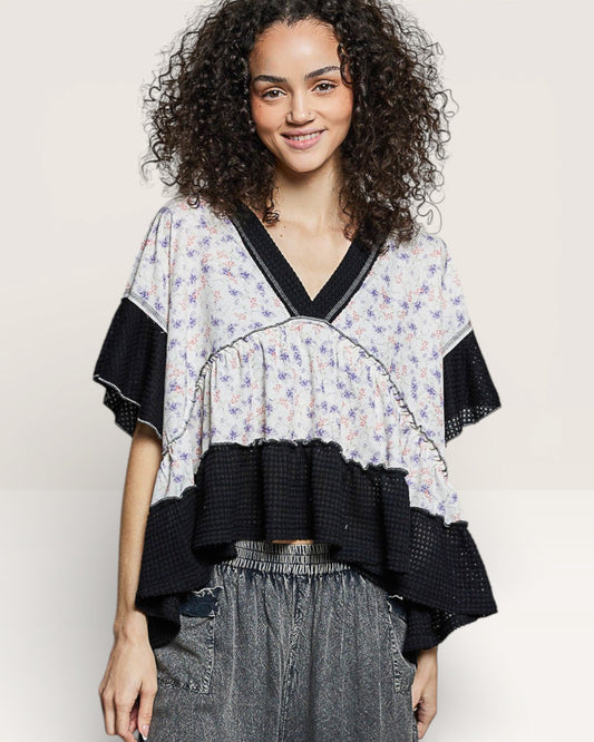 Woman wearing a floral blouse with black ruffled sleeves on a plain background