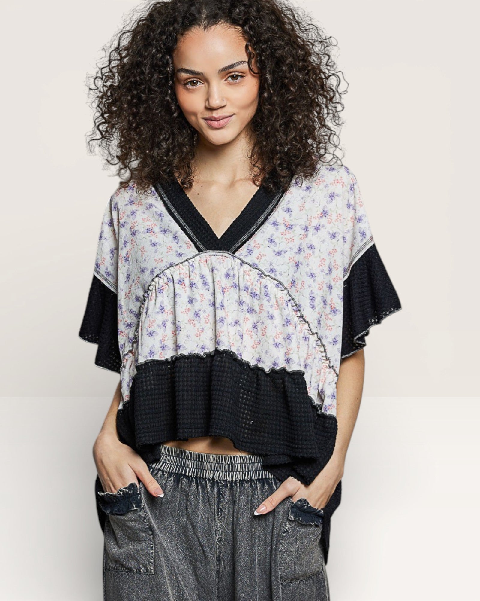 Woman wearing a layered top with floral and black designs on a plain background